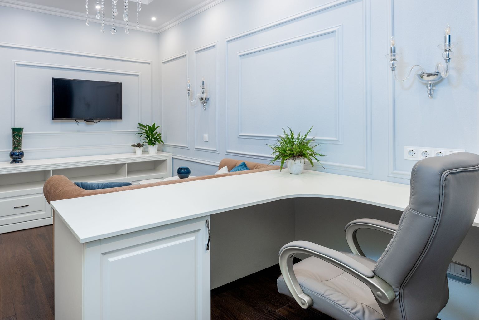 Luxurious office interior with minimalist design, featuring white furniture, chandelier, and flat-screen TV.
